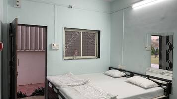 Een slaapkamer met een eenpersoonsbed, een plafondventilator, een raam met geblindeerde jaloezieën en een deur die leidt naar een buitenruimte.