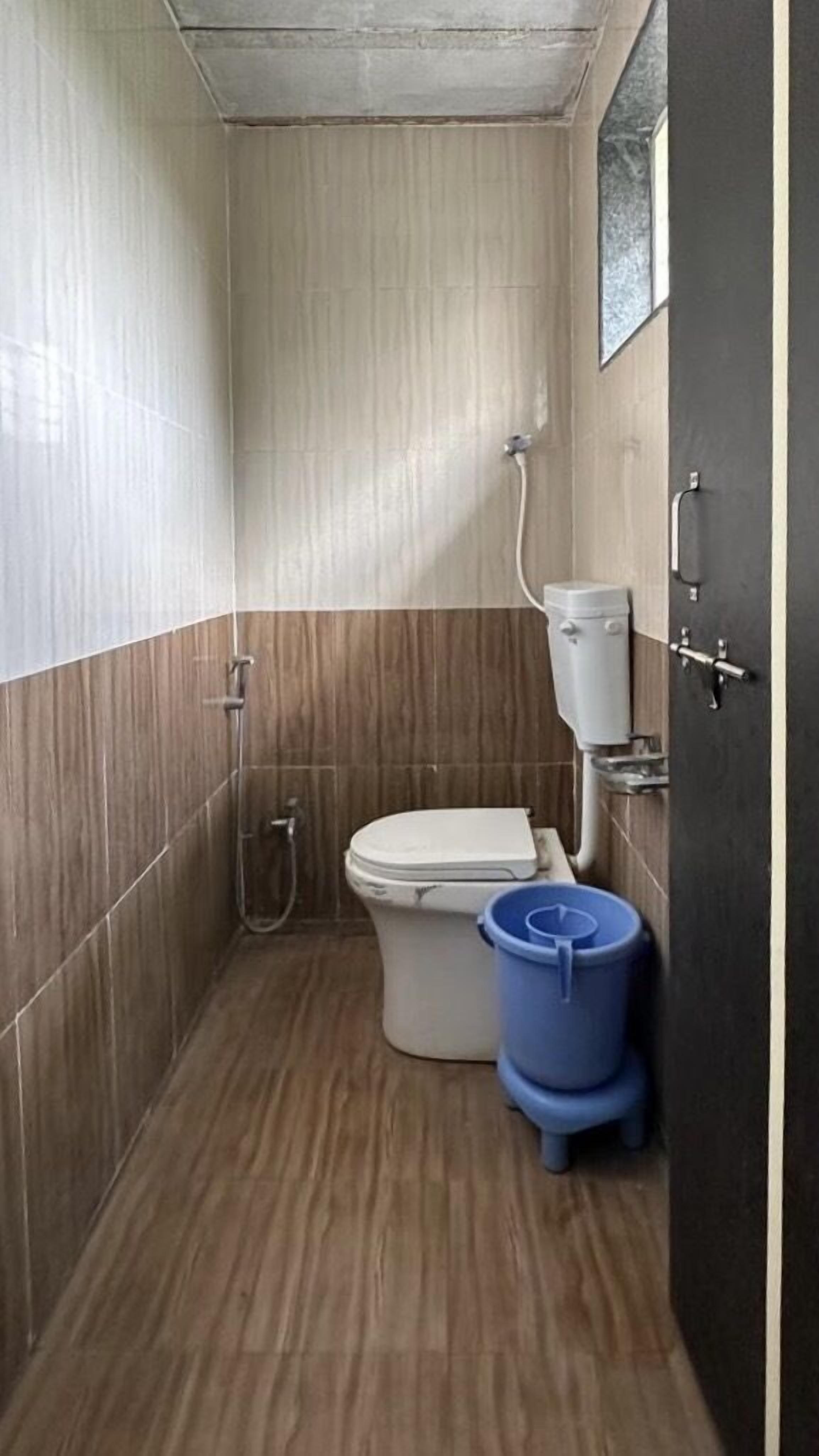 Un bagno piccolo e stretto, con il water, una doccia e un cestino blu.