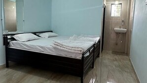 Un dormitorio con cama, ventilador de techo, baño con lavamanos y espejo.
