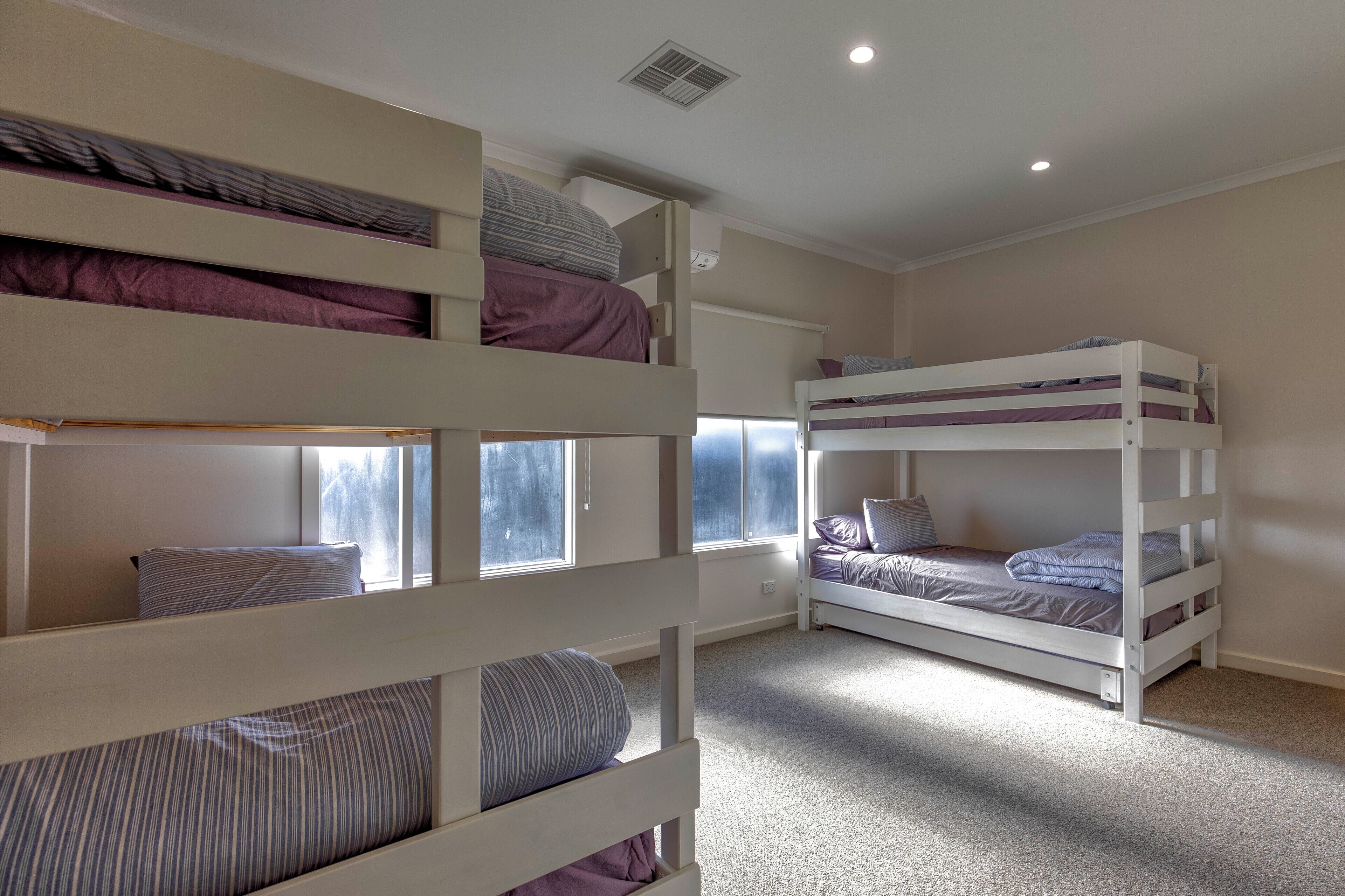 A bunk bed room with a window, a ceiling vent, and a carpeted floor.