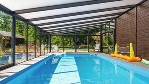 An indoor swimming pool with a glass enclosure, a covered roof, and a net for children.