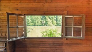 A wooden cabin room with a large window, wooden walls, and a bed with a white bedspread.