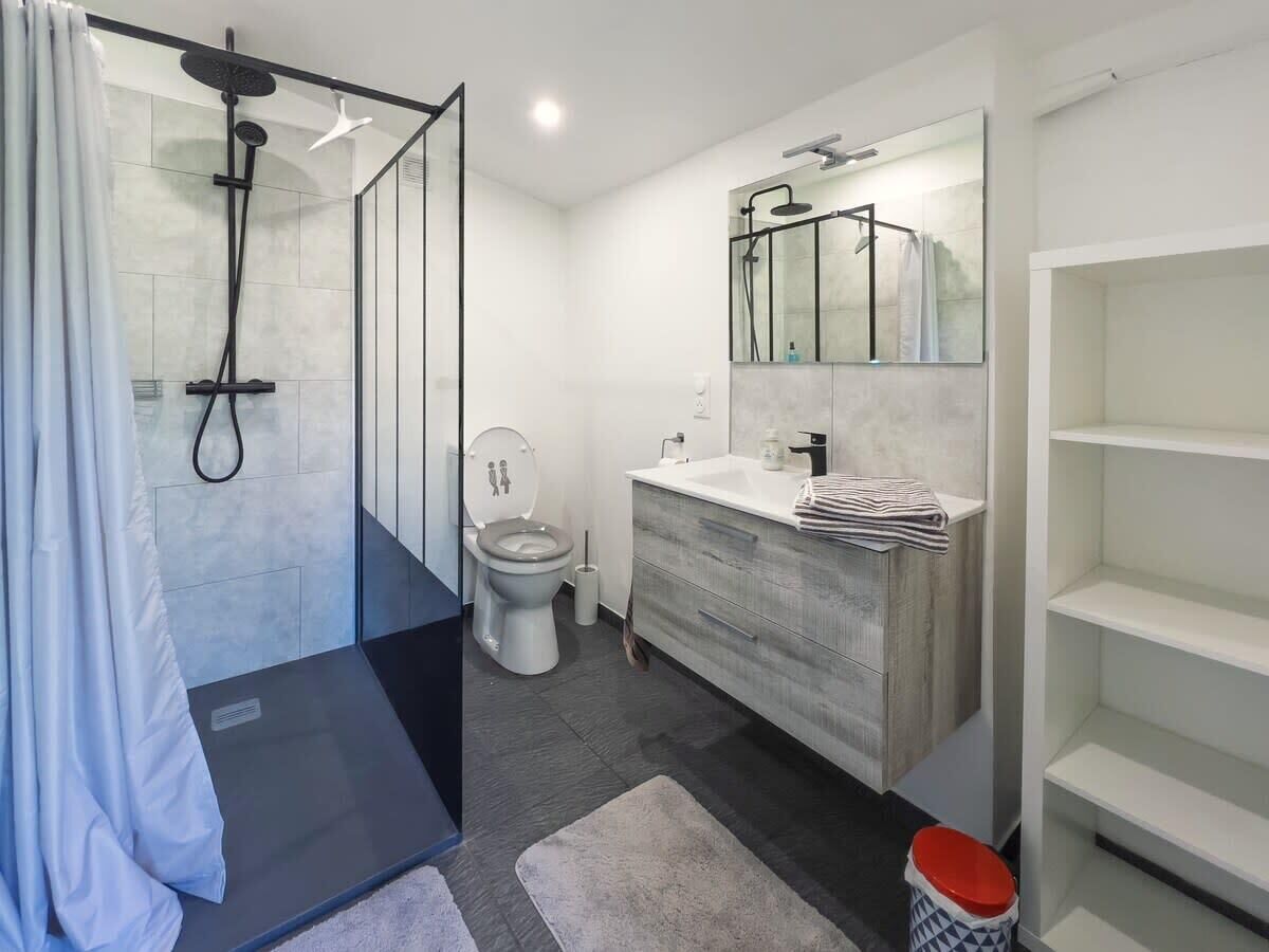 Une salle de bain moderne avec une douche à parois de verre, des toilettes, un meuble-lavabo avec un miroir et une étagère de rangement.