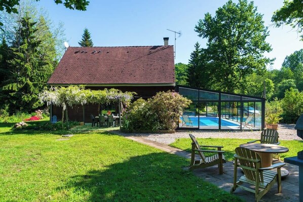 A house with a swimming pool, a patio with chairs, and a garden.