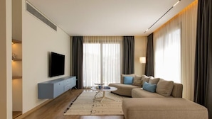 A modern living room with a sofa, ottoman, and a flat-screen TV on a wall. - Kennah Varenna | Silver Palm, New Cairo - Families Only (New Cairo)