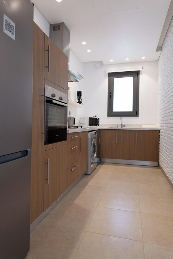 Une cuisine compacte avec des meubles en bois, un four encastré, un four à micro-ondes et un lave-linge.