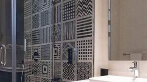 A modern bathroom with patterned tiles, a glass shower enclosure, a white toilet, and a marble sink. - Kennah Varenna | Silver Palm, New Cairo - Families Only (New Cairo)