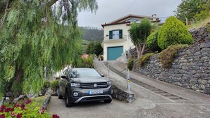 Um carro estacionado em uma entrada que leva a uma casa com muro de pedra e garagem.