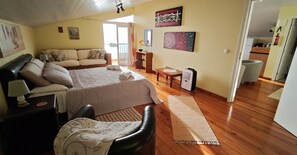 A bedroom with a bed, a desk, a chair, a sofa, and a balcony.