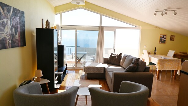 Uma sala de estar espaçosa com um sofá grande, duas poltronas, uma mesa de centro e um espaço de jantar com mesa e cadeiras.