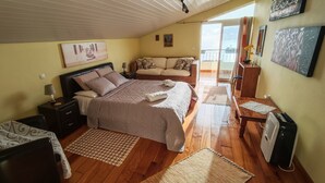 Quarto com cama, mesas de cabeceira, sofá, escrivaninha e janela com vista.
