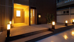 Una entrada de edificio moderna con fachada de madera, una puerta visible y luces del suelo iluminadas.
