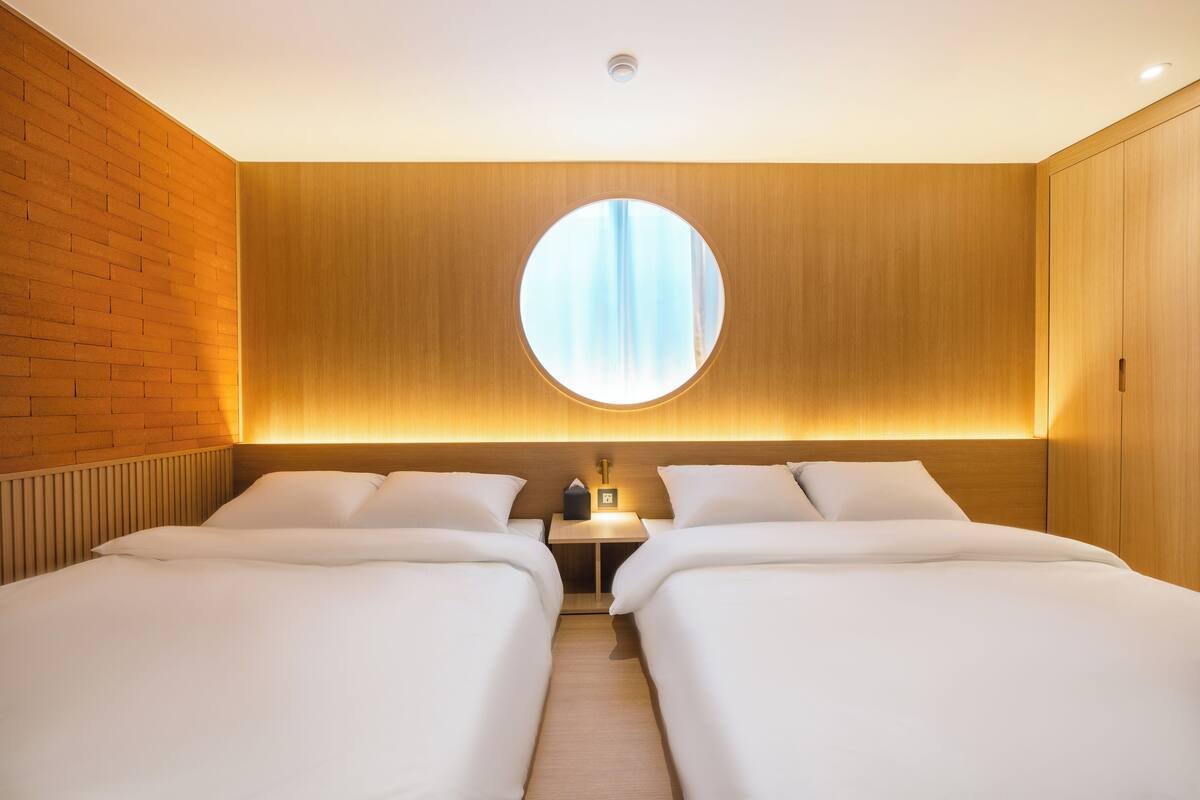 Ein Hotelzimmer mit zwei Betten, einem runden Fenster und einer Holzwand.