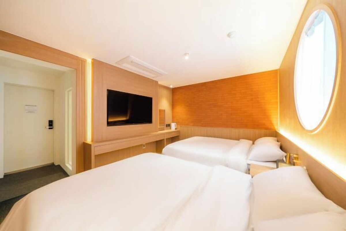Een hotelkamer met twee bedden, een aan de muur bevestigde televisie en een ronde spiegel.