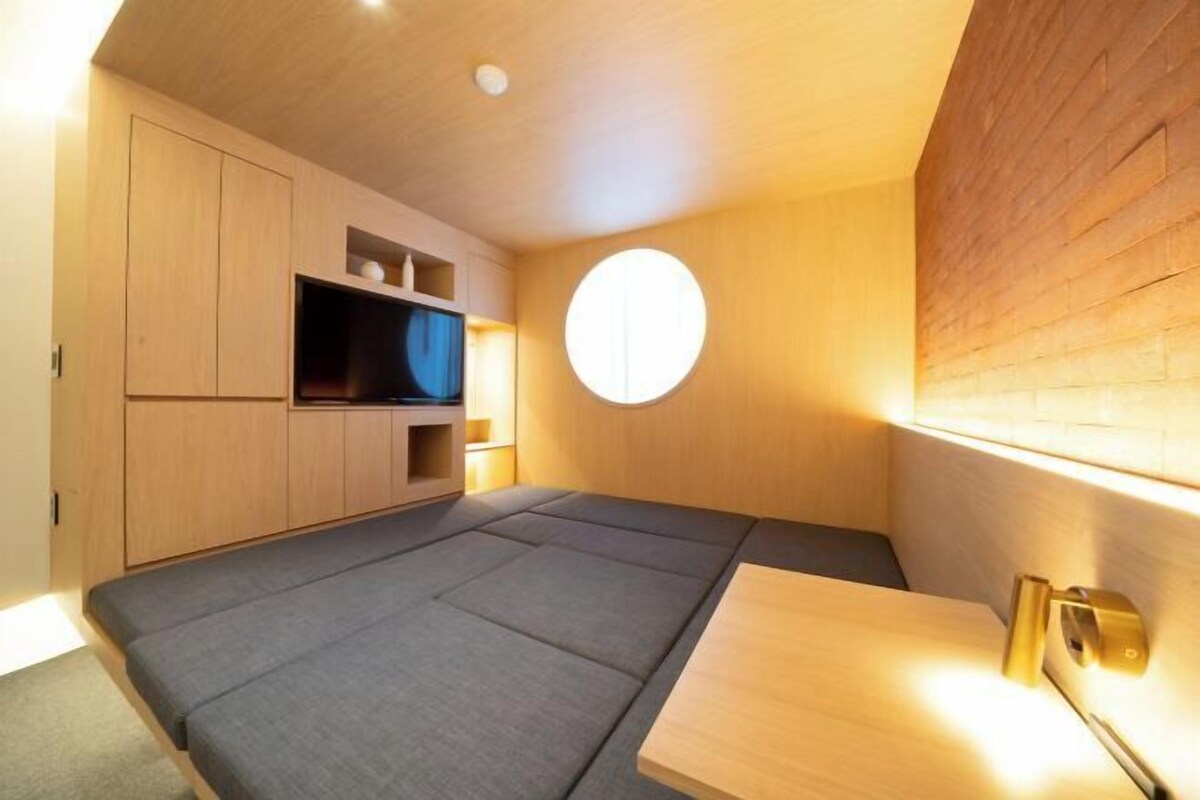 Een compacte kamer met een bed, een klein tafeltje en een televisie op een houten kast.