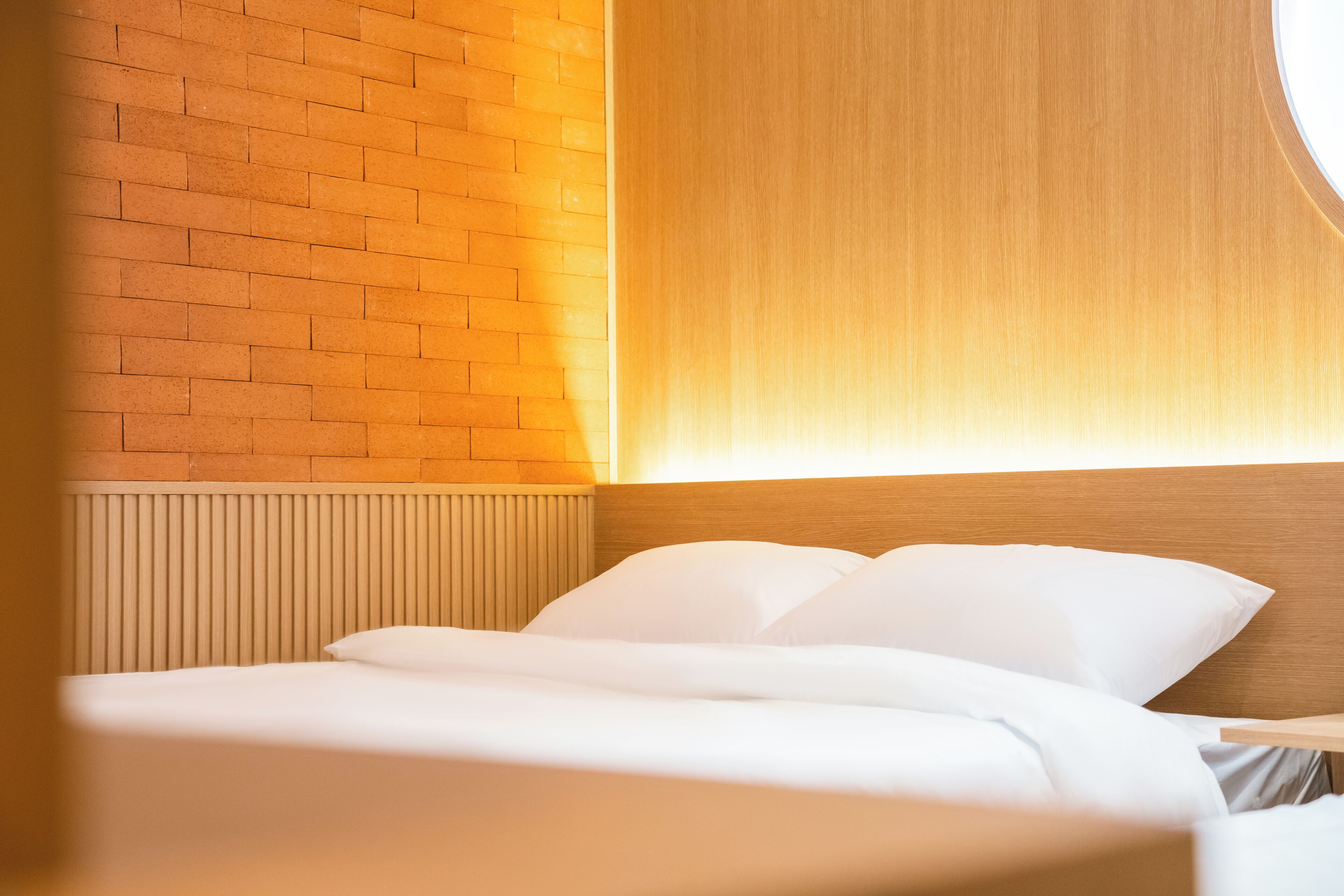 Habitación de hotel con pared de ladrillo, cabecero de madera y cama con ropa blanca.