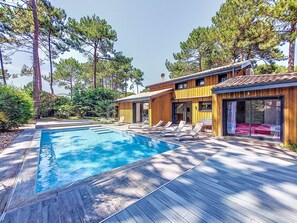 Ett modernt hus med en swimmingpool, ett trädäck och en uteplats med solstolar.