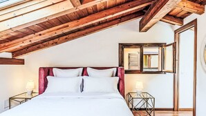 A bedroom with a sloped wooden ceiling, a large bed with white bedding, two bedside tables with lamps, and a mirror on the wall. - Borgo Castello by Interhome (Argegno)