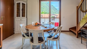 Un comedor con una mesa redonda, cuatro sillas, un frutero y vistas a un paisaje montañoso a través de un amplio ventanal.