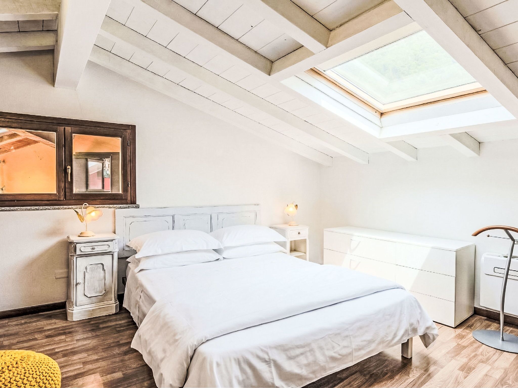 A bedroom with a skylight, a bed, a bedside table, a wardrobe, and a floor lamp.