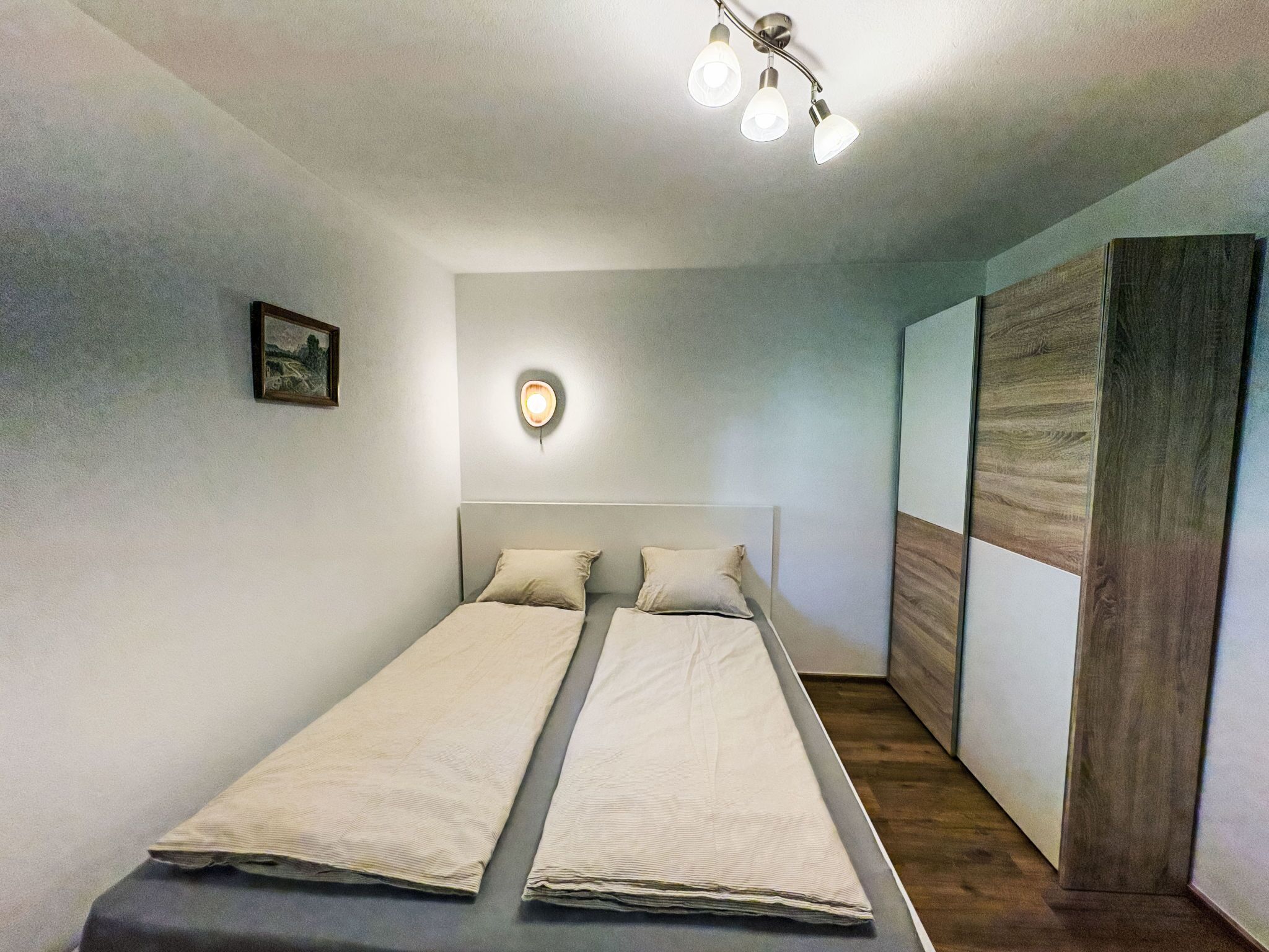 A double bed with a headboard, a wall-mounted light, and a wooden panel on the right.