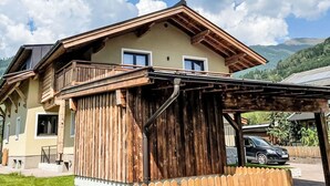 Een chalet met twee verdiepingen, een houten balkon, een overdekte veranda en een berg op de achtergrond.