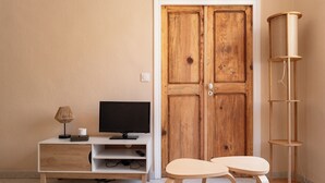 A room with a wooden door, a white TV stand with a flat-screen TV, a small table, and a tall cat tree. - Cosy cocoon in the heart of Bastia (Bastia)