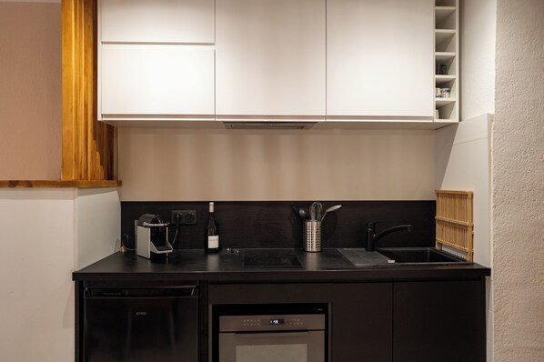 Cocina compacta con lavavajillas integrado, una botella de vino y una tetera sobre la encimera.