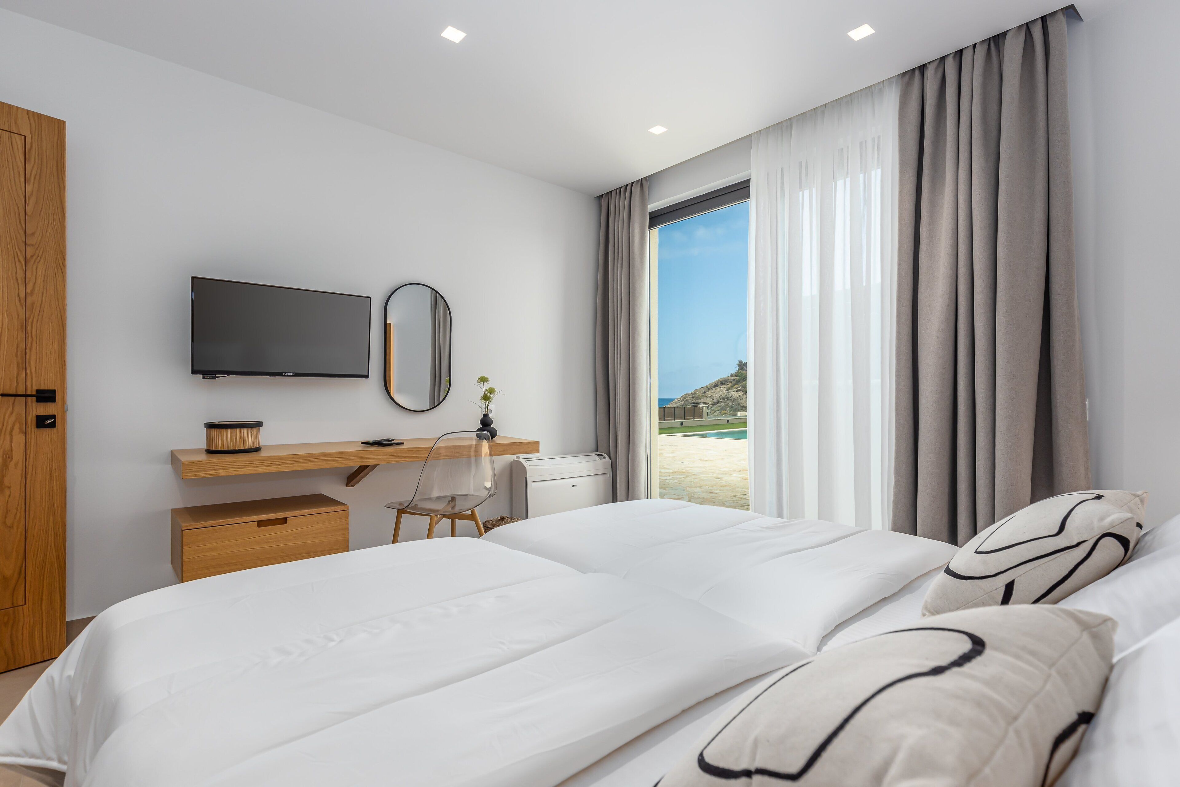 Une chambre d’hôtel moderne dotée d’un grand lit, d’un bureau avec un téléviseur à écran plat, d’un miroir et offrant une vue sur la plage.
