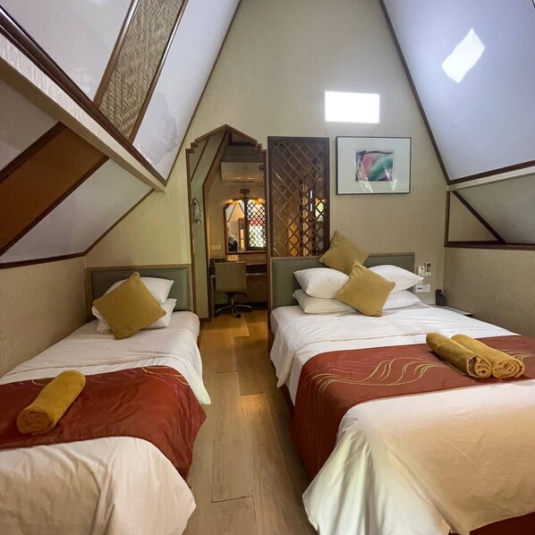 Habitación triangular con dos camas, cada una con cabecera, un escritorio pequeño y una ventana.