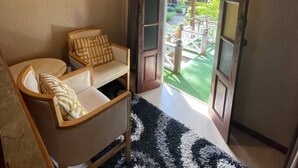 A cozy room with a wooden sofa, a black and white rug, and a large window with a view of a garden and a blue building outside. - Coralview Resort BlueStar - Perhentian (Pulau Perhentian Besar)