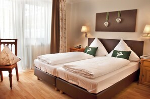 A double bed with two pillows, a wooden chair, a nightstand with a lamp, and a wall-mounted decoration.