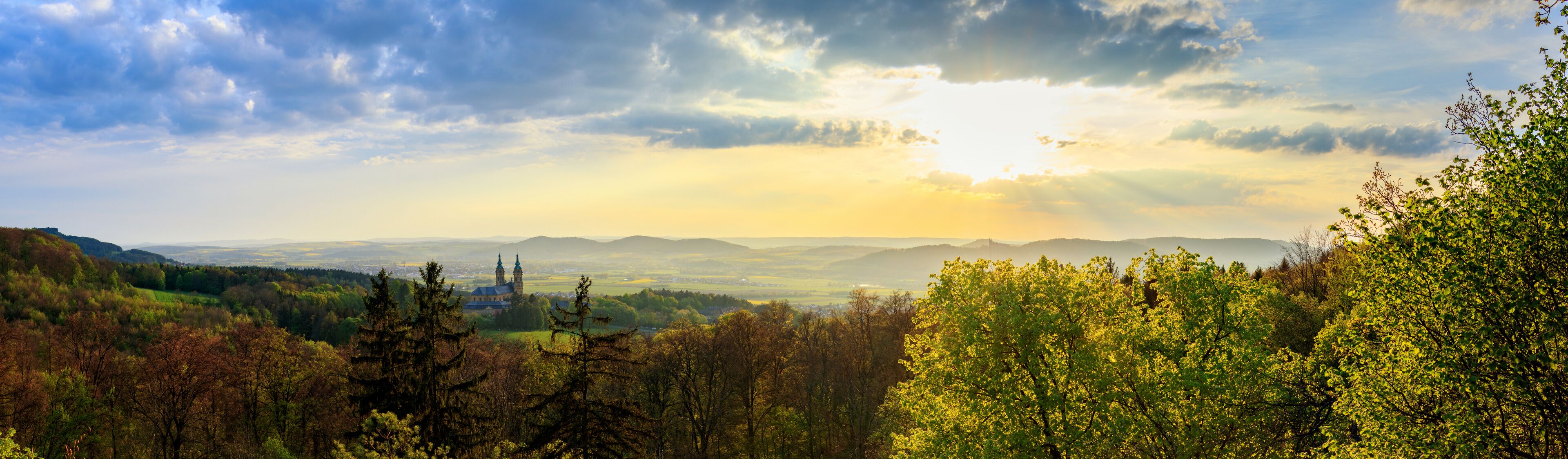 Ein weiter Panoramablick auf ein Tal mit einer markanten Kirche und sanften Hügeln im Hintergrund.