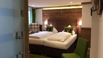 Un dormitorio con cabecera de madera, dos camas con sábanas blancas, una silla verde y una silla a cuadros.