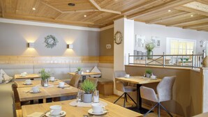 A cozy restaurant with wooden tables and benches, a clock on the wall, and a view of the kitchen through a window. - Landhotel Augustin (Staffelstein)