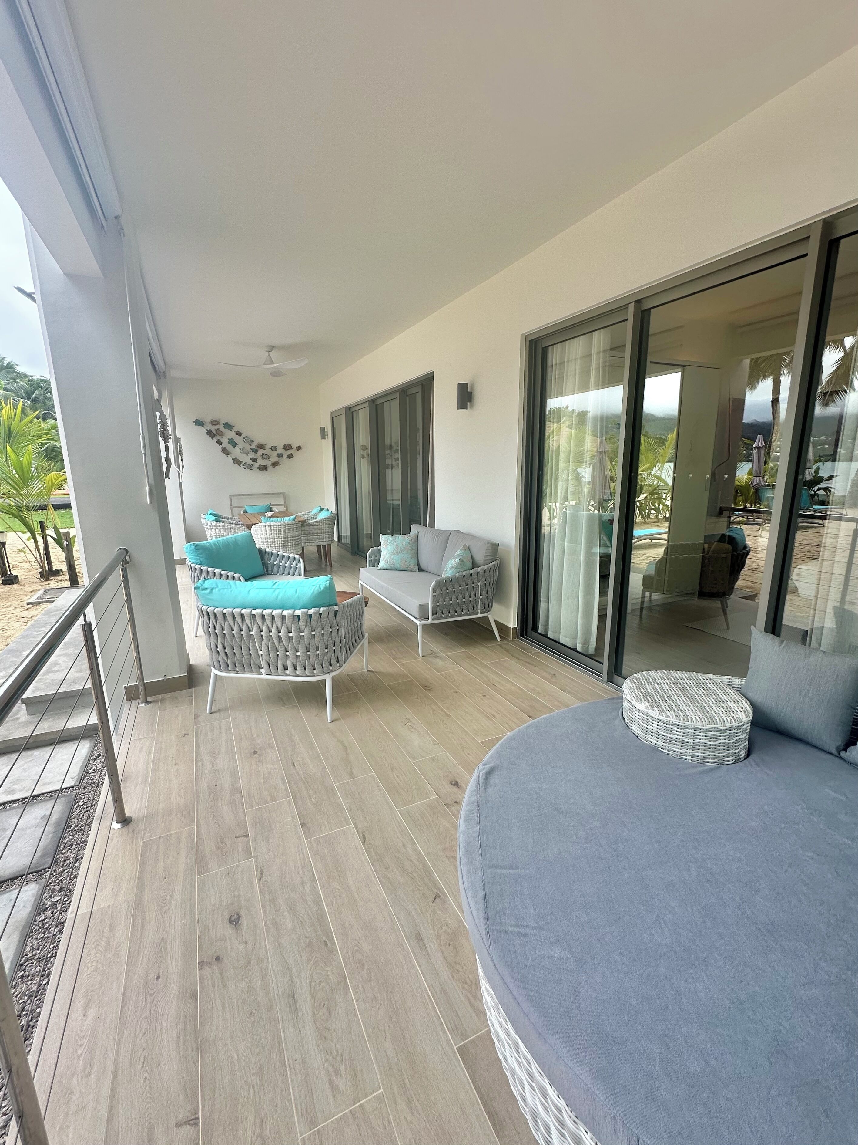 A spacious balcony with wicker furniture, a grey sofa, and a view of the outdoors.