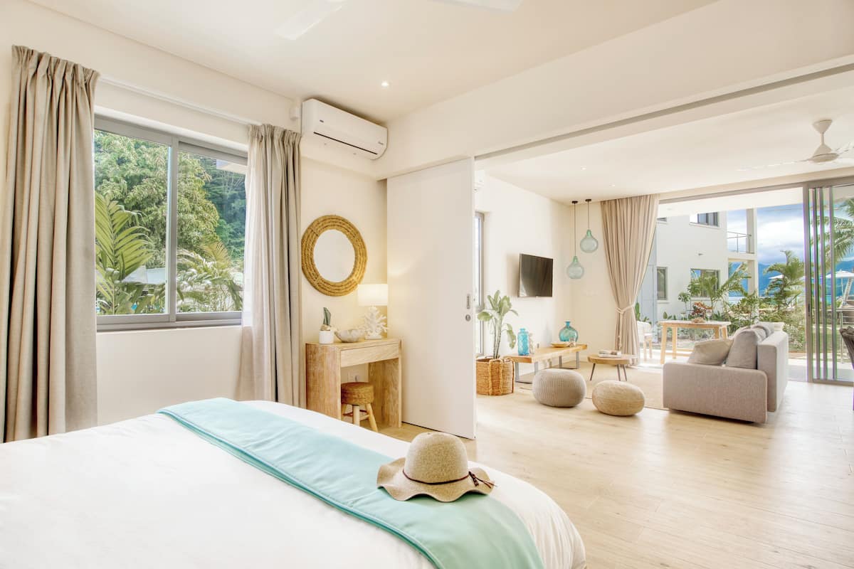 Une chambre d’hôtel moderne dotée d’un grand lit, d’un bureau, d’un canapé et d’un balcon offrant une vue sur l’océan.