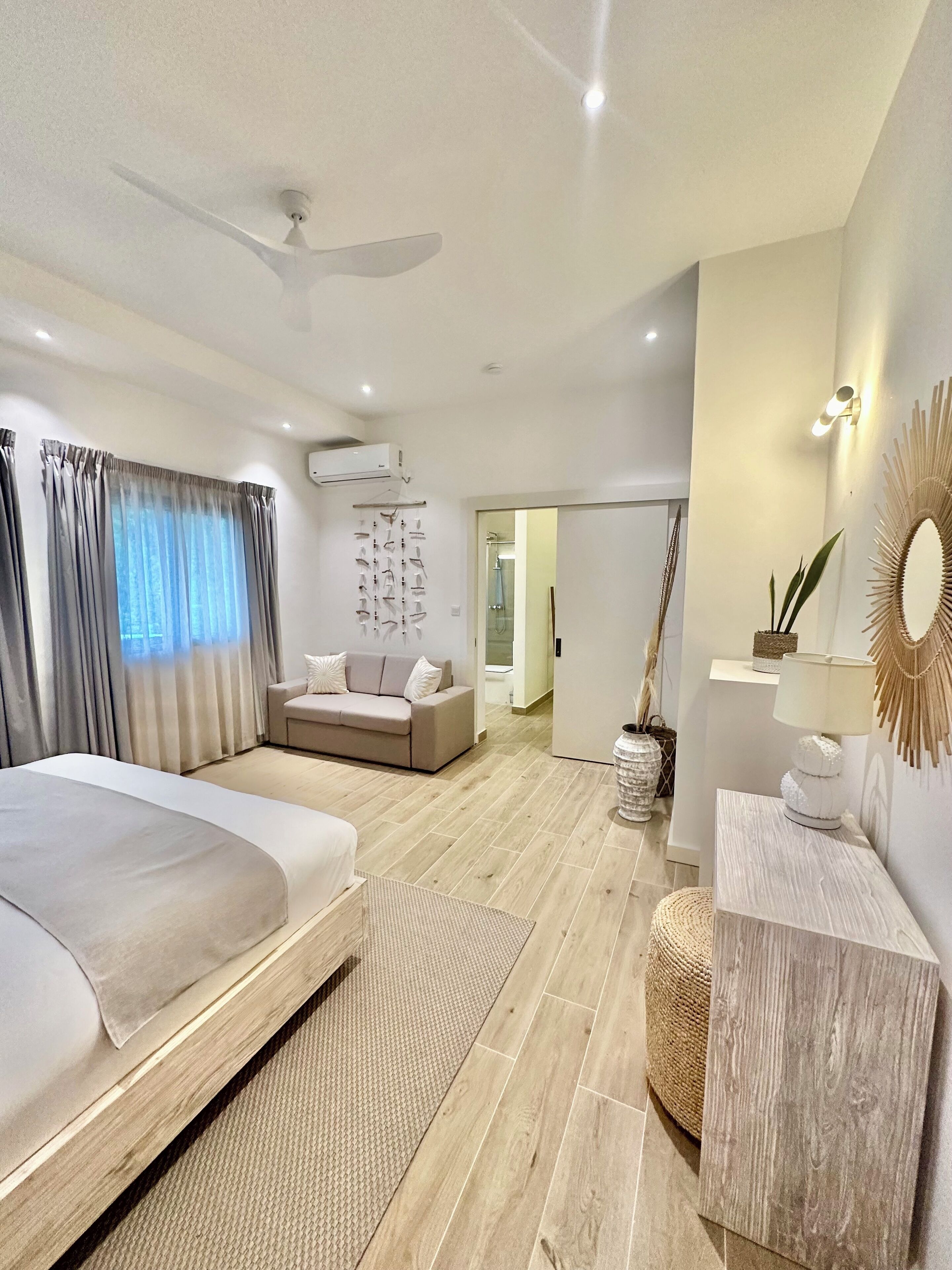 A modern bedroom with a large bed, a sofa, a ceiling fan, and a wall-mounted air conditioner.