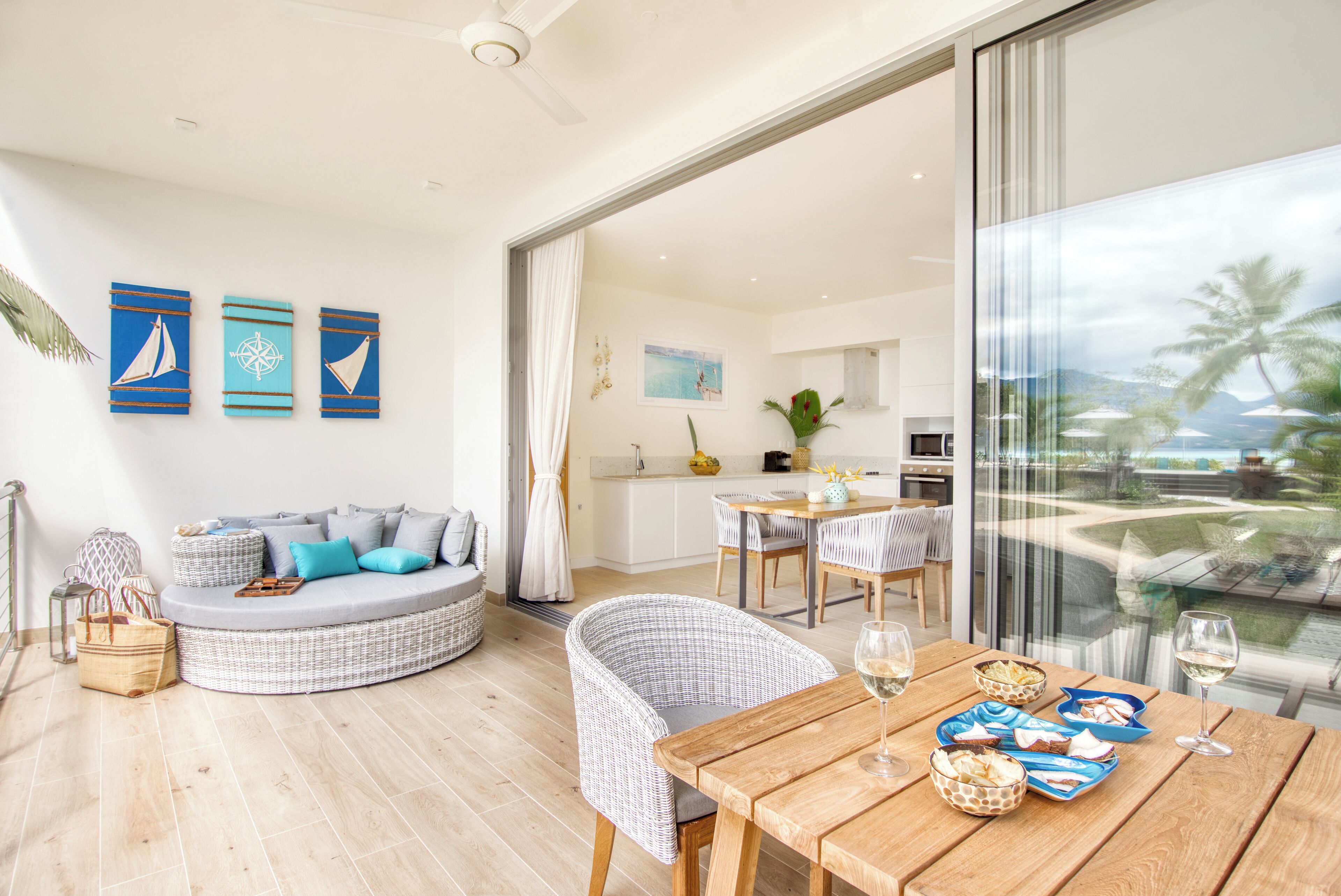 Ein modernes Wohnzimmer mit einer gebogenen Couch, einem Esstisch mit Stühlen und Blick auf die Küche sowie den Außenbereich durch große Fenster.
