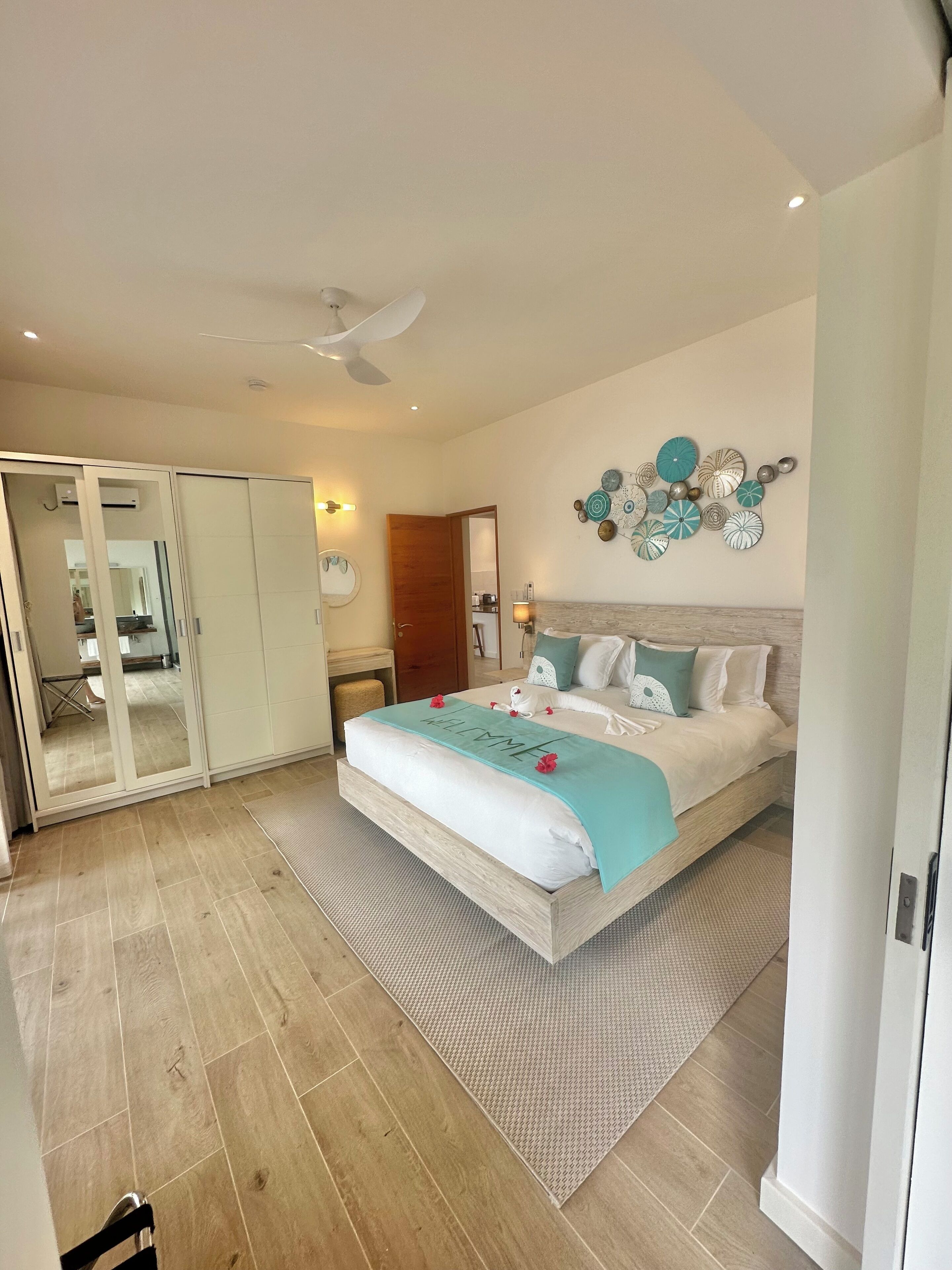 A spacious bedroom with a large bed, a ceiling fan, and a wall-mounted decorative piece.