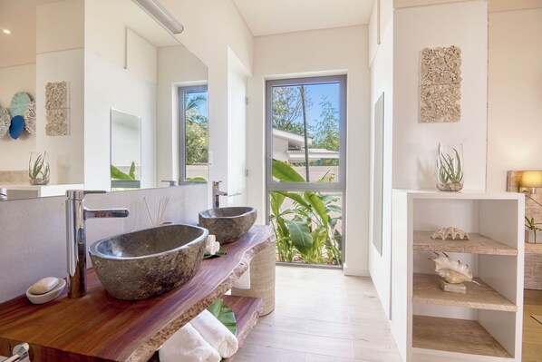 A modern bathroom with a large mirror, two stone sinks, and a wooden vanity.
