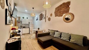 A modern living room with a sectional sofa, a dining table, and a kitchen in the background. - WAKAFLATS 1, CHUECA SB (Madrid)