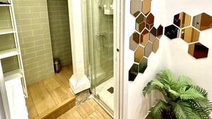 A modern bathroom with a glass shower enclosure, a white tiled shower area, and a hexagonal mirror wall decoration. - WAKAFLATS 1, CHUECA SB (Madrid)