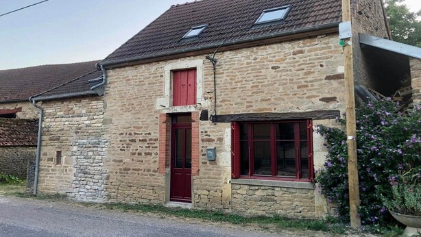 Un edificio in pietra con una porta rossa, finestre, un camino e una piccola finestra sul tetto.