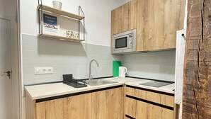A compact kitchen with wooden cabinets, a microwave, a sink, and a coffee maker. - WAKAFLATS 2 CHUECA SB (Madrid)