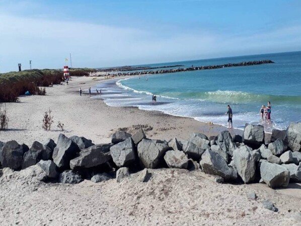 A beach with rocky foreground, a sandy shore, and a calm sea.