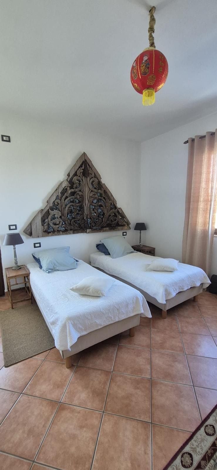 A hotel room with two beds, a decorative headboard, a hanging lantern, and a tiled floor.