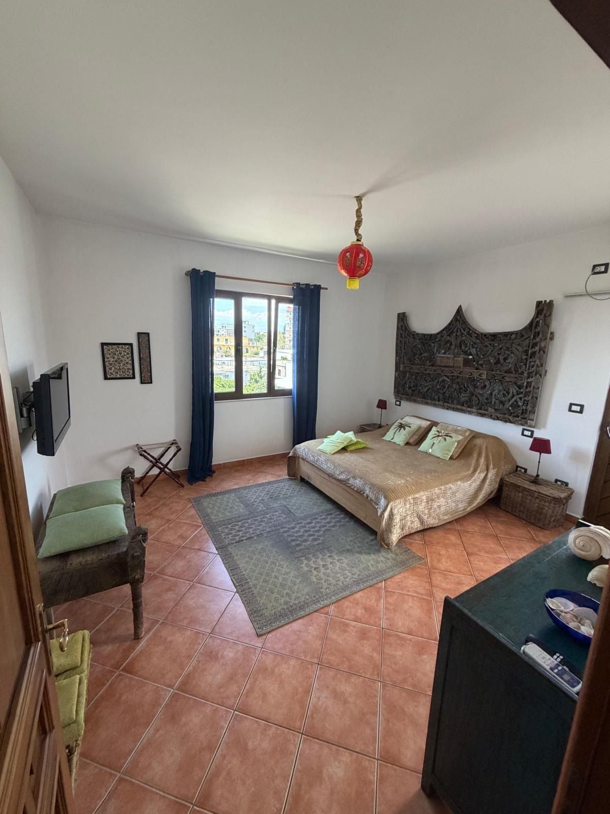 A bedroom with a bed, a desk, a chair, a window with curtains, a hanging lantern, and a decorative wall piece.