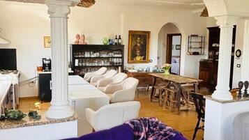 Una sala de estar con un sofá morado, un comedor con mesa de madera y una cocina con armarios blancos.
