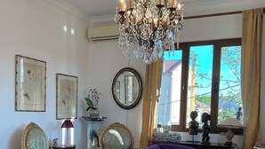 Un salon avec un canapé violet, un lustre et une vue sur l’extérieur grâce à de grandes fenêtres.